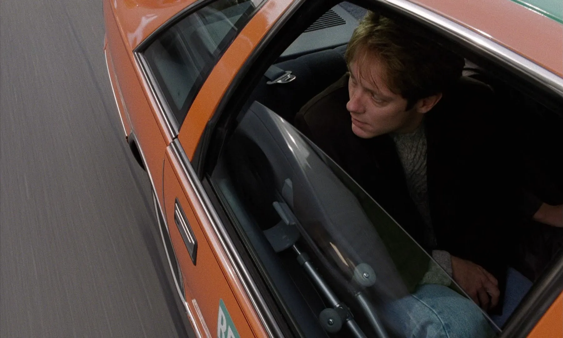 A man in the back seat of a small car, looking out the window